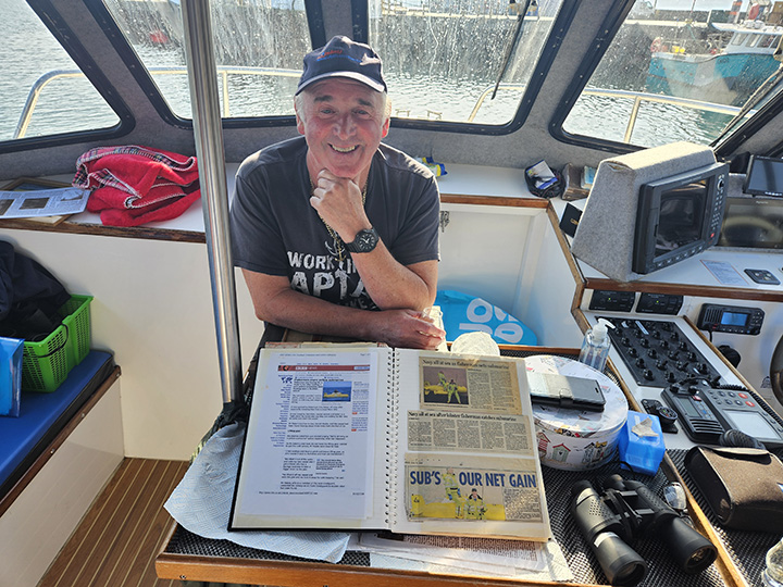 Harold Hastie auf seinem Boot, vor ihm ein Album mit Zeitungsausschnitten